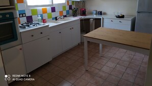 Eine Küche mit weißen Schränken, einer gefliesten Spritzschutzwand, einem Holztisch und einem Fenster mit Vorhängen.