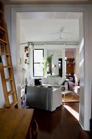 Un salon spacieux avec un canapé blanc, une table en bois et un ventilateur de plafond.