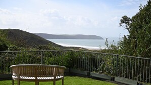 A wooden bench on a grassy lawn overlooking a coastal landscape with hills and a view of the sea. - 5 Bed in Woolacombe (oc-bella) (Woolacombe)