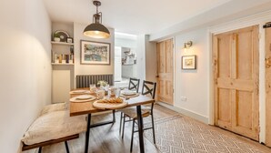 A dining area with a wooden table, chairs, a bench, a hanging light fixture, a radiator, and a patterned rug.