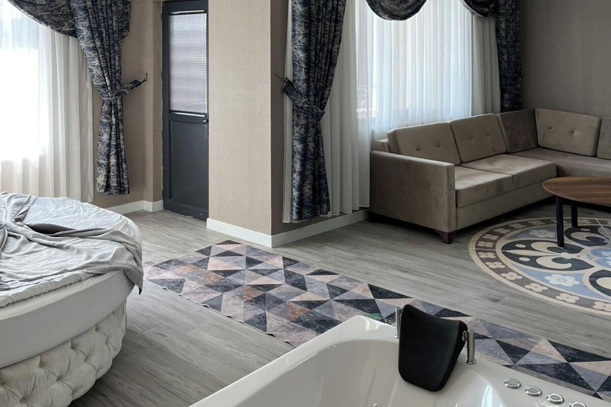 A modern living room with a sofa, a round coffee table, a bed, and patterned curtains.
