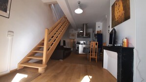 A modern apartment with a wooden staircase, a kitchen area, a dining table, and a living room.