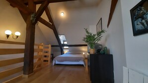 A bedroom with a wooden ladder, a bed, a desk, and a potted plant.