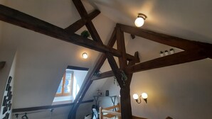A room with exposed wooden beams, a window with blinds, a small table with a plant, and a chair.
