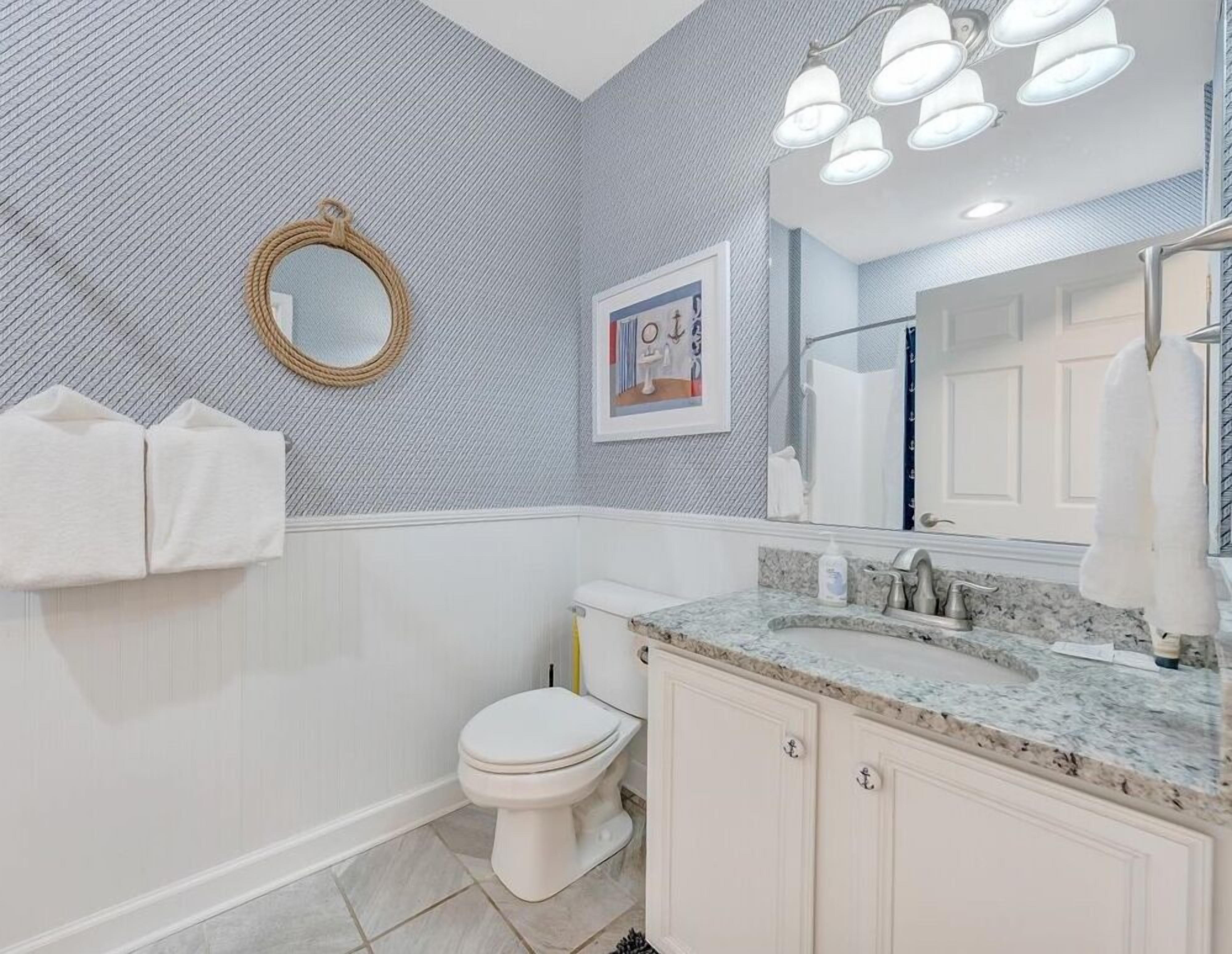 Un bagno con servizi igienici, lavandino e specchio. C'è un porta asciugamani con asciugamani, un quadro appeso al muro e una parete strutturata.