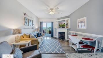 A modern living room with a sofa, a dining table with chairs, a fireplace, and a ceiling fan.