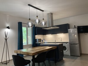 Cozinha moderna com mesa de madeira, cadeiras pretas, forno embutido e máquina de lavar.