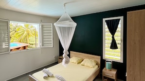 Une chambre à coucher avec un lit en bois, un lit à baldaquin, une petite table de chevet et une vue sur une piscine à l’extérieur.