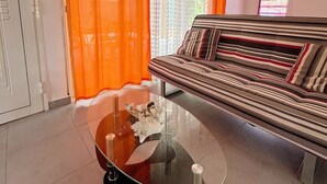 Un salon avec une table basse en verre, des rideaux orange, un canapé à rayures et une fenêtre avec des stores.