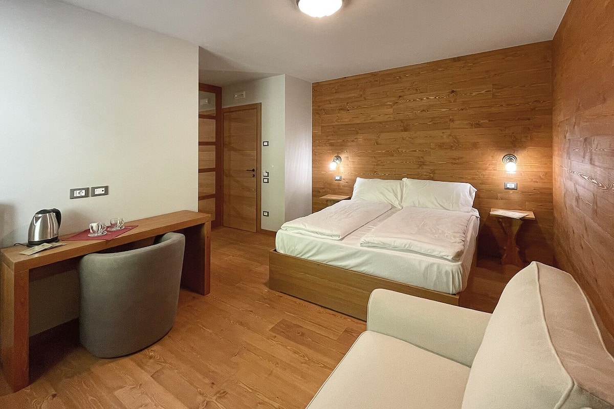 Una habitación compacta con cama, escritorio y silla. Hay dos mesitas de noche con lámparas.