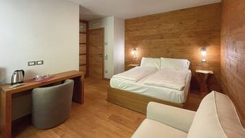 A compact hotel room with a wooden wall, a bed with white bedding, a desk with a chair, and a small bedside table.