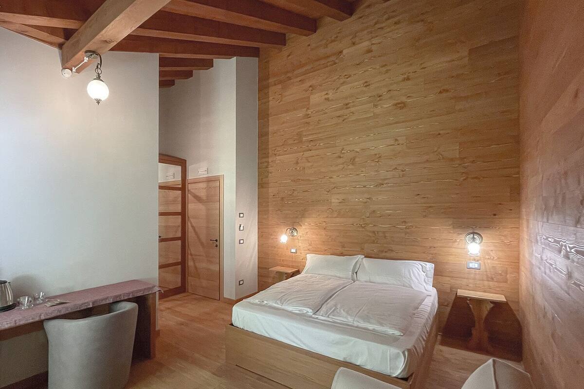 Un dormitorio con techo de madera, una cama, mesitas de noche y un escritorio con silla.