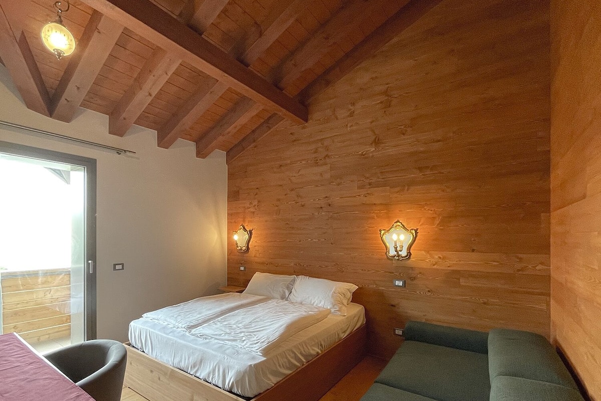Un dormitorio con techo de madera, una cama, un sofá verde y dos lámparas de pared.