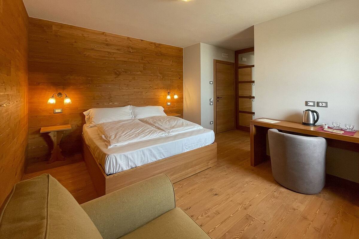 Una habitación de hotel moderna con un panel de madera decorativo, una cama con ropa blanca, un escritorio con hervidor y una silla.