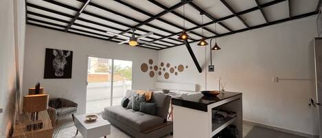 A modern living room with a grey sofa, a white coffee table, and a kitchen area with a black countertop.