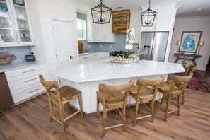 Una cocina amplia con una isla grande, sillas de madera, armarios blancos y una lámpara moderna.