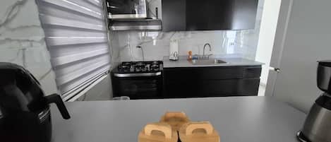 A modern kitchen with a gas stove, sink, and black cabinets. There is a flat-screen TV mounted above the stove.