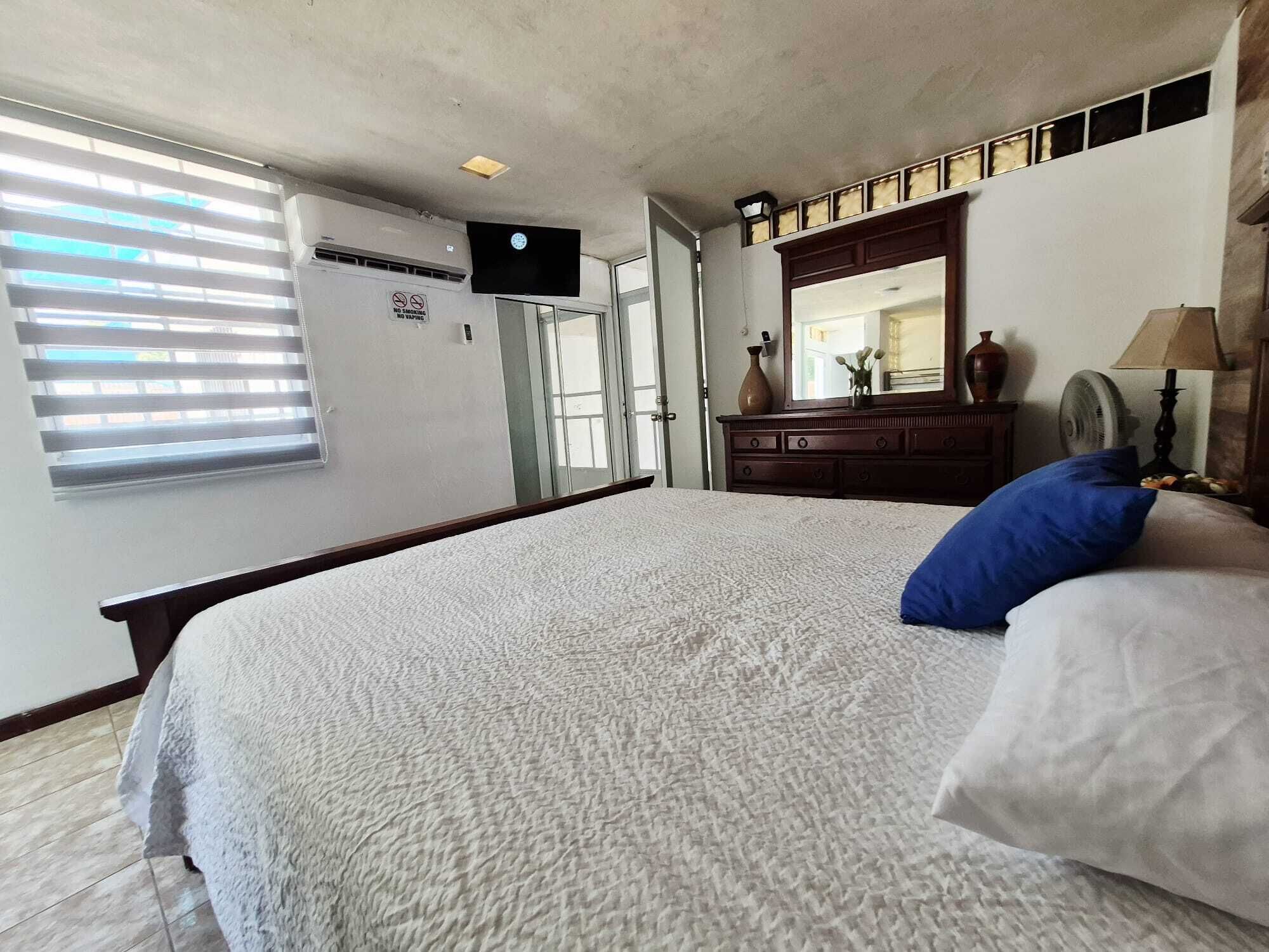 A bedroom with a bed, a dresser, a mirror, and a window with blinds.