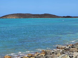 A coastal scene with clear turquoise water, rocky shoreline, and a distant hill. - Cozy Corner w/ Private Pool, Pool Table, A/C, Wi-Fi, Laundry & Parking (Vega Baja)