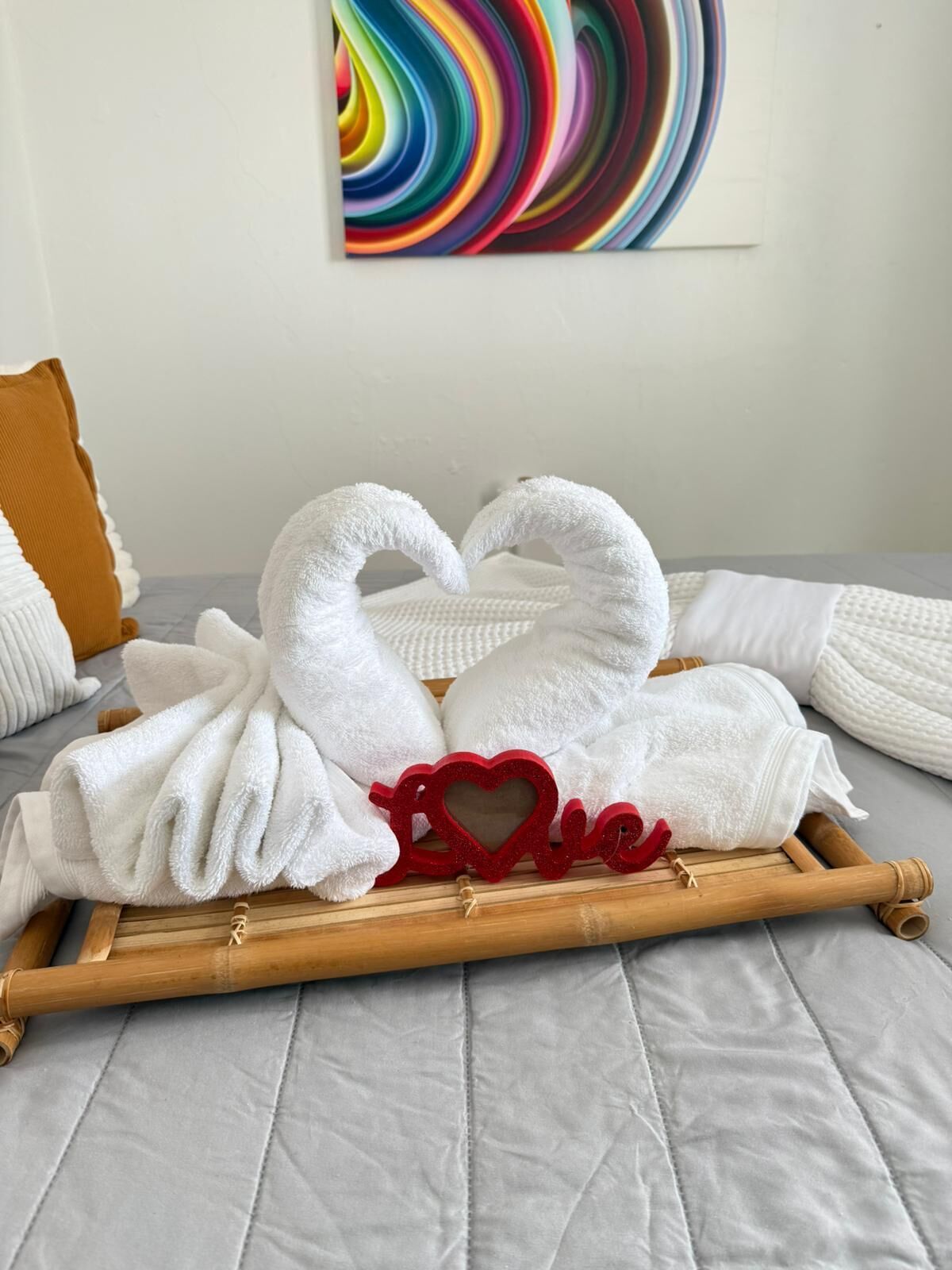 Ein Bett mit weißen Handtüchern, die zu einem Herz geformt sind, einer roten herzförmigen Dekoration und einem farbenfrohen abstrakten Gemälde an der Wand.