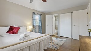 A bedroom with a bed, a ceiling fan, a window with curtains, a door, and a wooden floor.