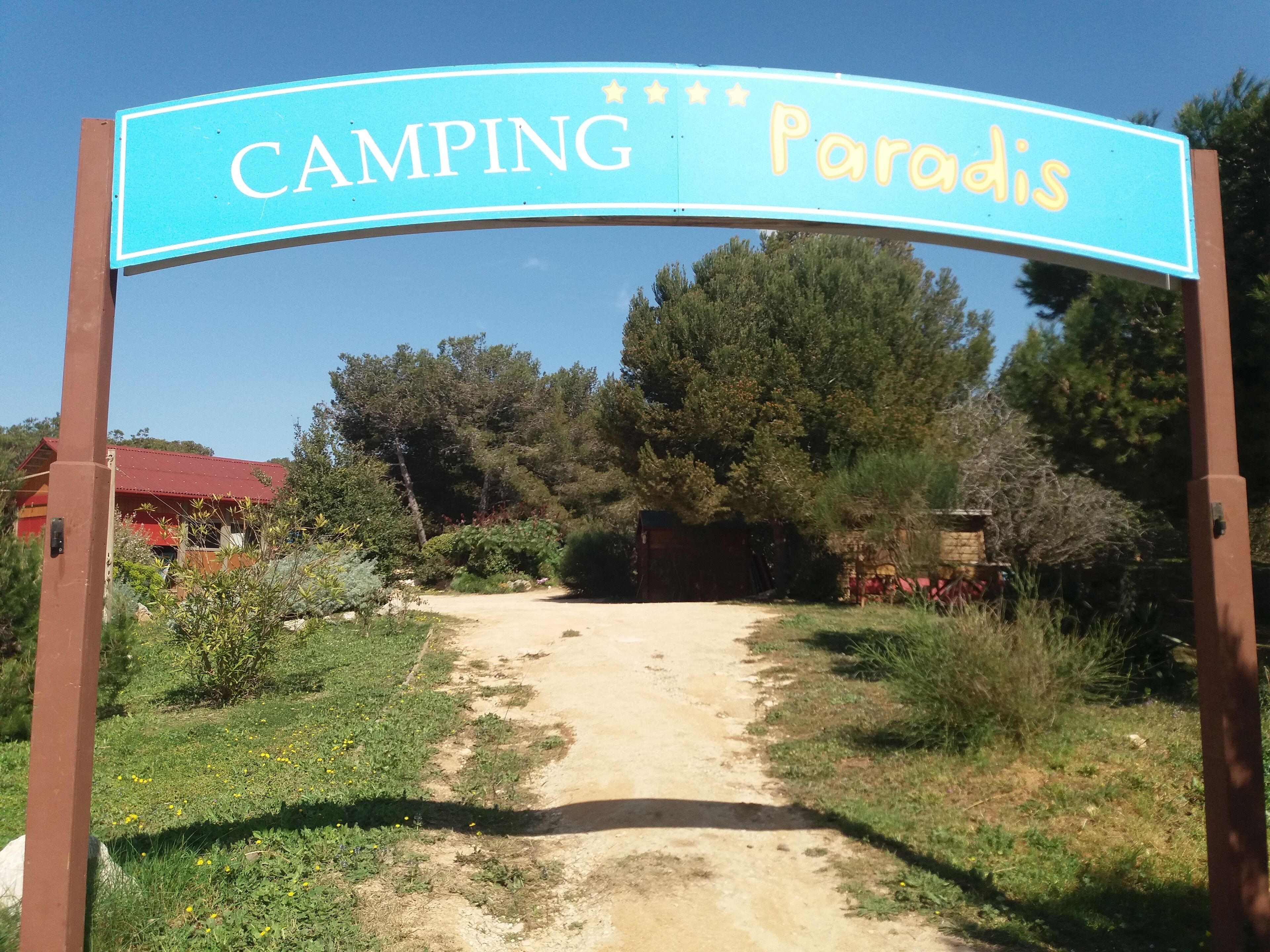 A sign reading "CAMPING Paradise" with a dirt path leading to a building.
