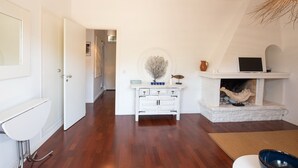 Una habitación con una mesa consola blanca, una chimenea, una computadora portátil y una puerta que da a otra estancia.