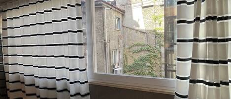 A room with a view of buildings outside, a window with striped curtains, and a sofa.