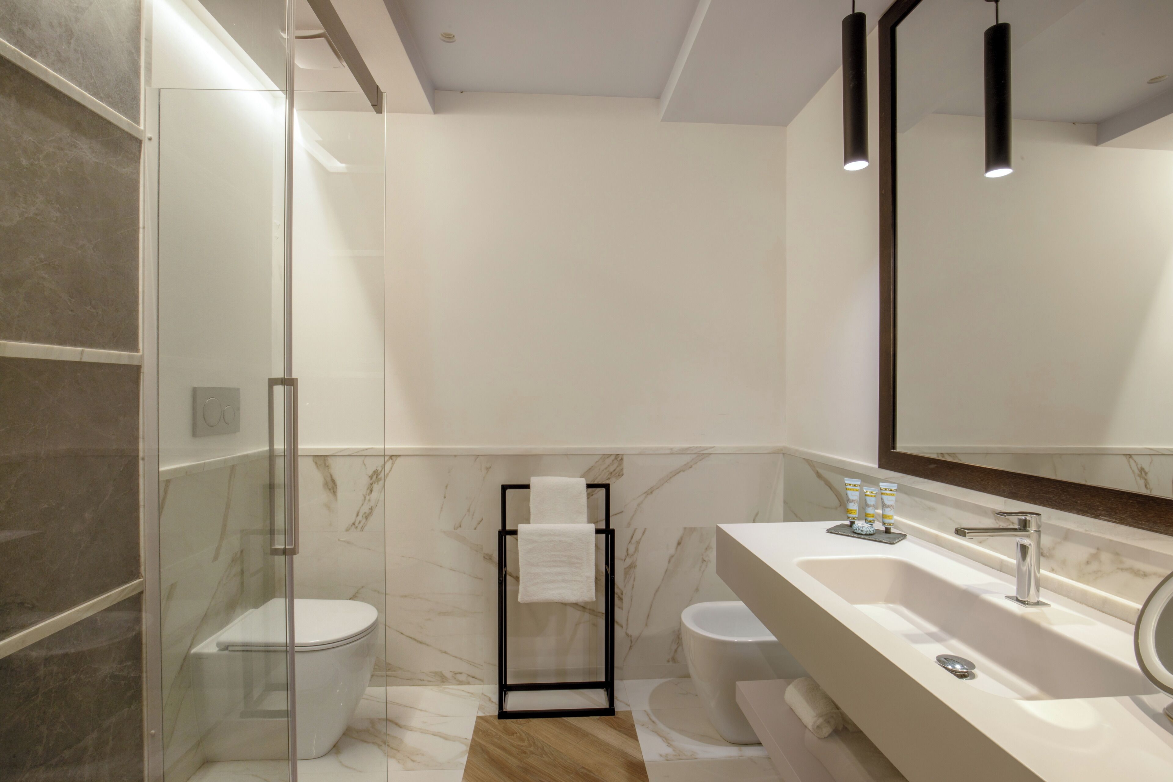 A modern bathroom with a glass shower enclosure, a white toilet, a sink with a mirror, and a towel rack.