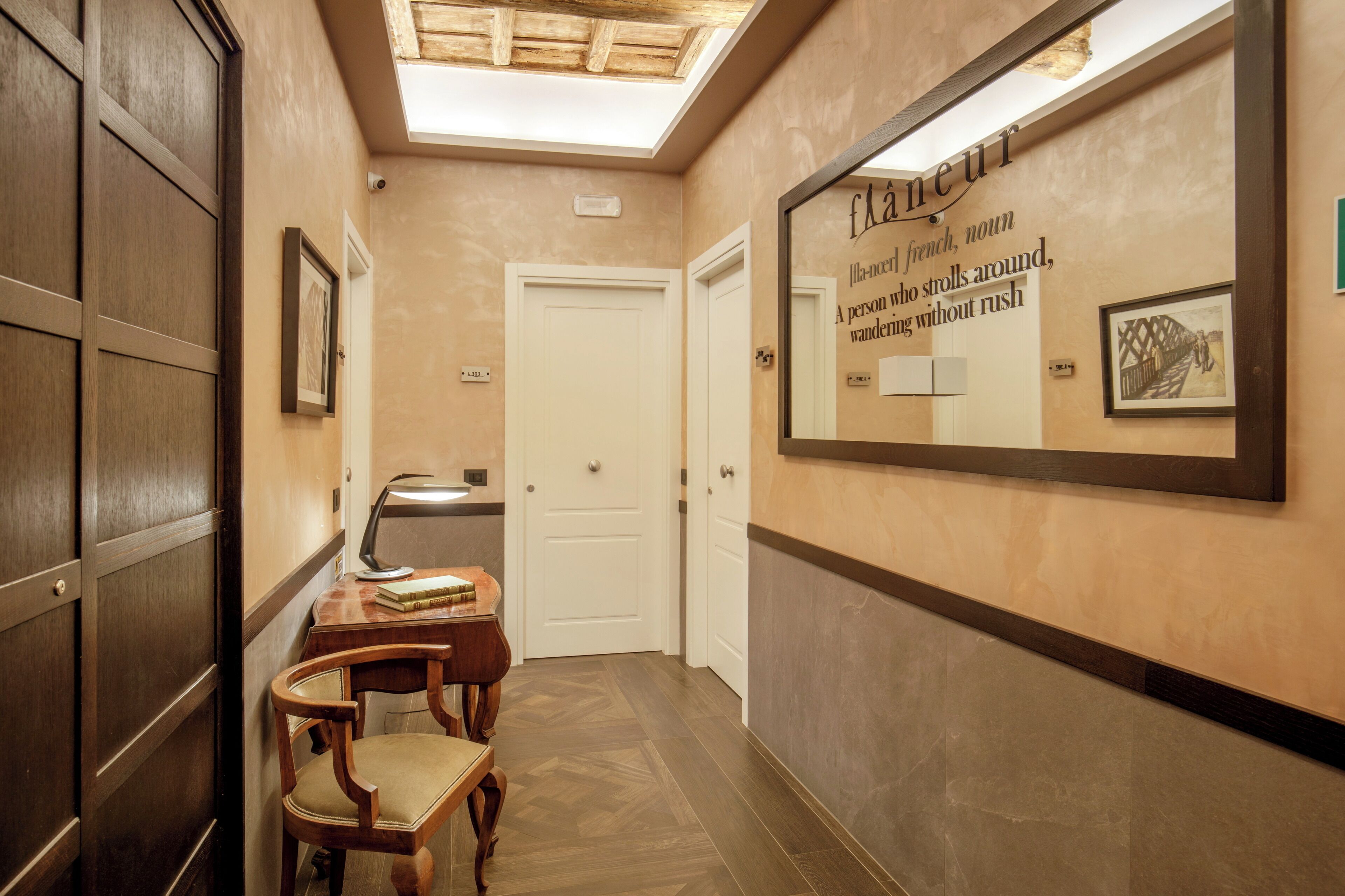 Un pasillo con puertas de madera, un escritorio con lámpara y una pared con una cita enmarcada.