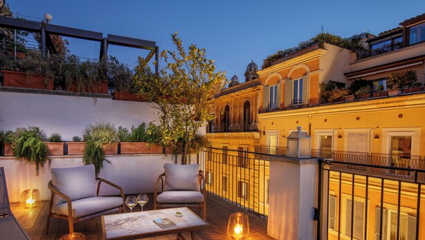 Une terrasse en bois avec deux chaises et une table, entourée d’une rambarde et agrémentée de plantes en pot.