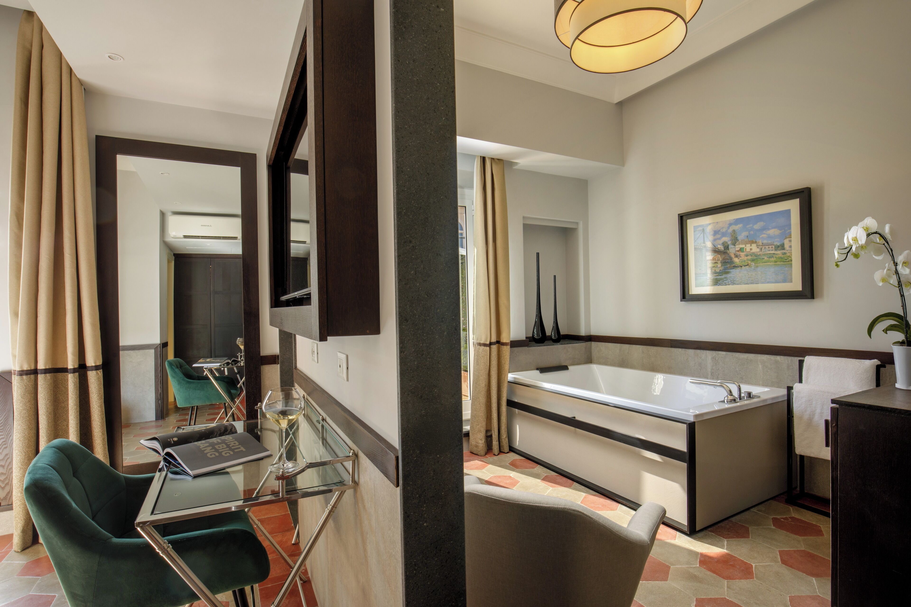 A modern hotel room with a glass table, a green chair, a large bathtub, and a framed picture on the wall.