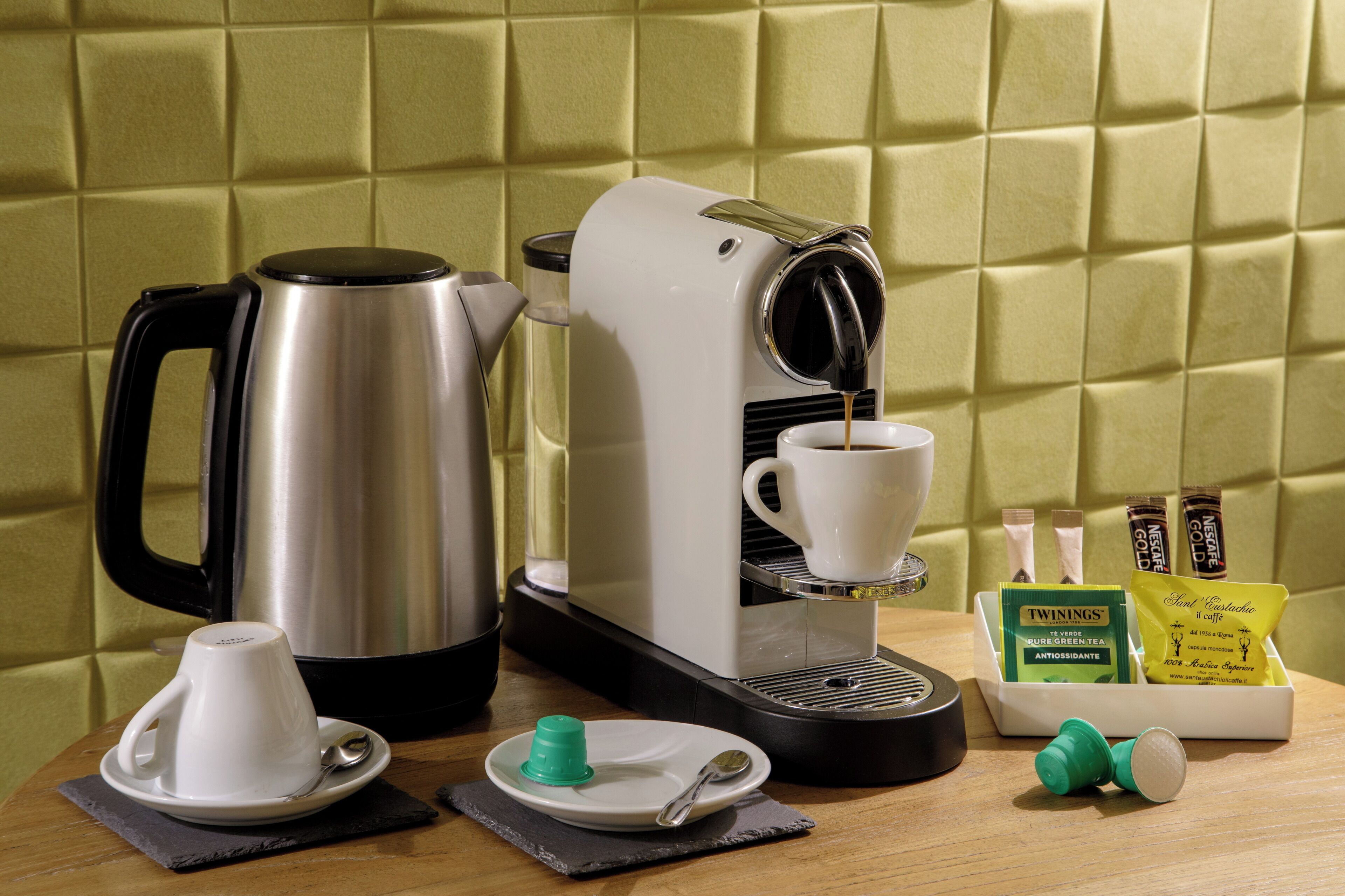 A coffee machine, a cup, a spoon, a green bottle, and a tray with coffee pods.