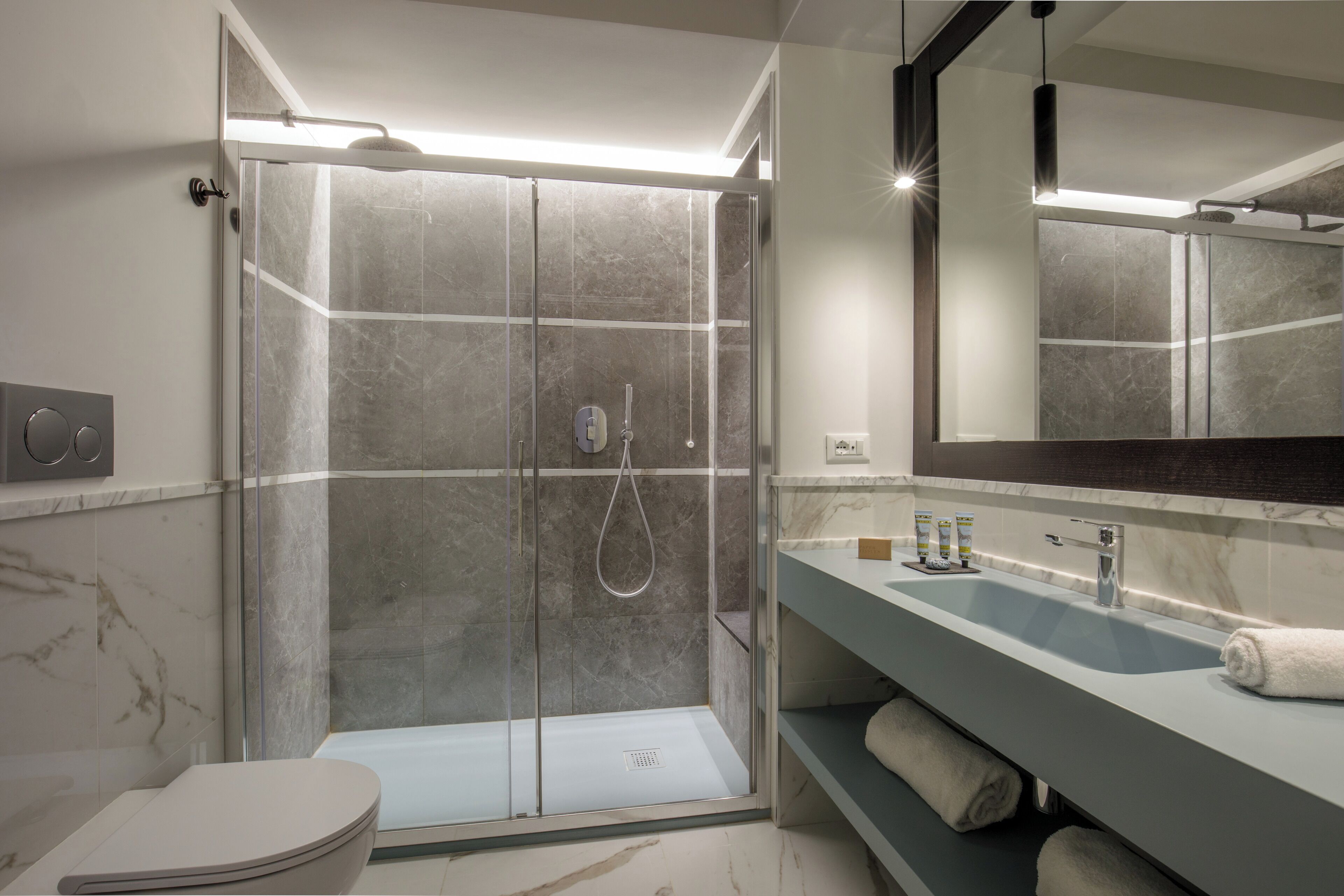Un baño moderno con cabina de ducha de vidrio, pared revestida de mármol, lavamanos con espejo y un inodoro.