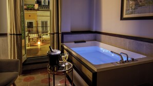 Une salle de bain moderne avec une grande baignoire, une petite table ronde agrémentée d’une bougie et de verres, et une vue sur la ville à travers une porte vitrée.