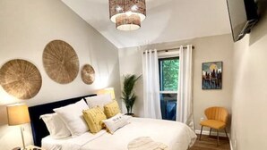 A bedroom with a bed, a nightstand, a lamp, a television, a chair, and a window with curtains. - Dreamy Cottage Getaway w/ Sunset Lakeview (Cadiz)