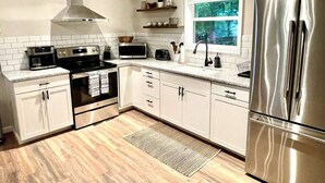 A modern kitchen with white cabinets, stainless steel appliances, and a window with a view of trees. - Dreamy Cottage Getaway w/ Sunset Lakeview (Cadiz)