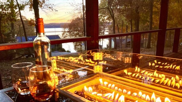 A dining area with a view of trees and a body of water. There are glasses and a bottle on the table. - Dreamy Cottage Getaway w/ Sunset Lakeview (Cadiz)