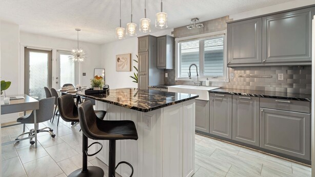 Una cocina moderna con una isla central, luces colgantes y un comedor con sillas.