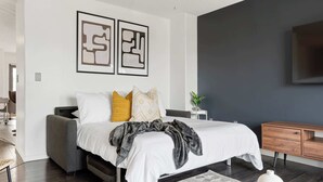 Un dormitorio moderno con cama, mesitas de noche, televisor y una obra de arte en la pared.