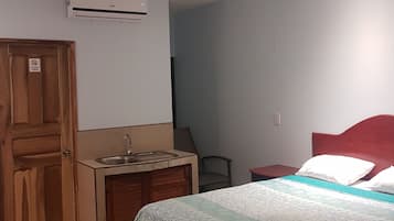 A bedroom with a bed, a ceiling fan, a sink, and a door.