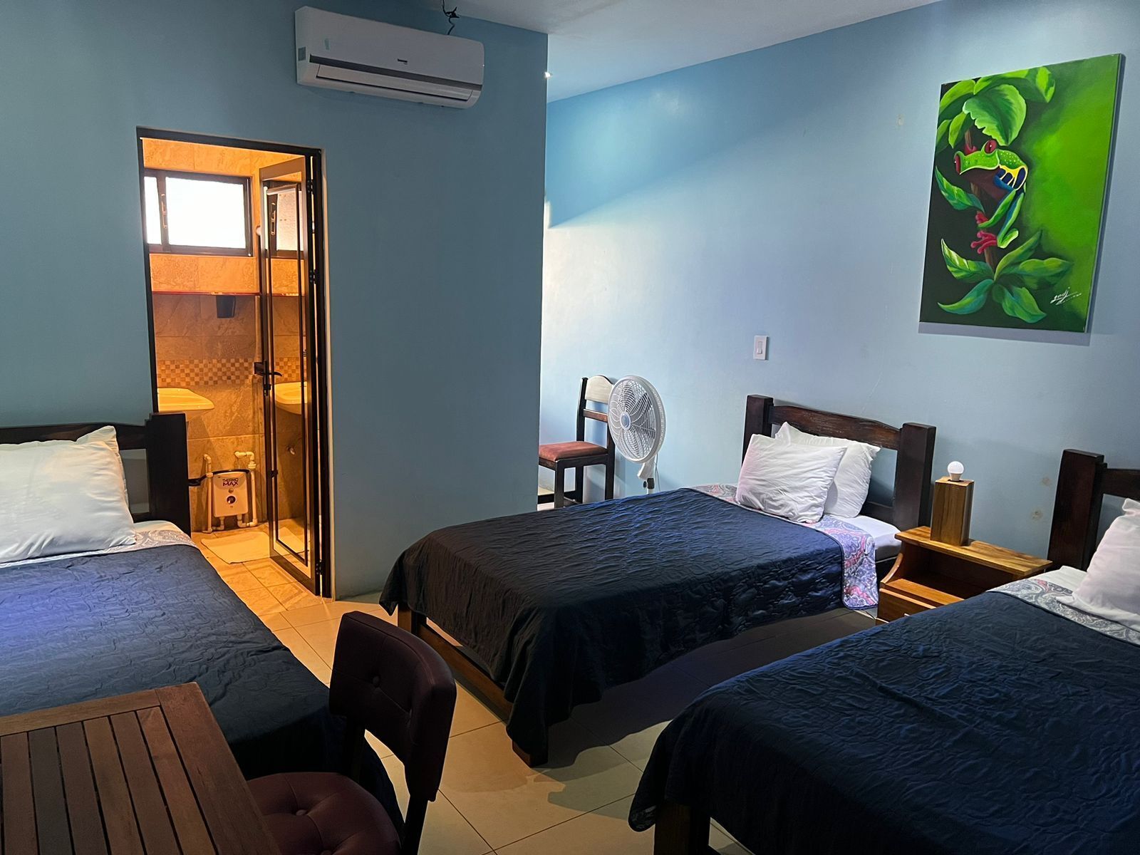 A hotel room with two beds, a sitting area, a fan, and a painting of a frog.