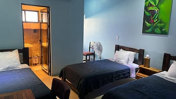 Una camera d'albergo con due letti, un'area salotto, un ventilatore e un quadro di una rana.