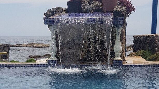 Piscina com elemento aquático, incluindo uma fonte e plantas.