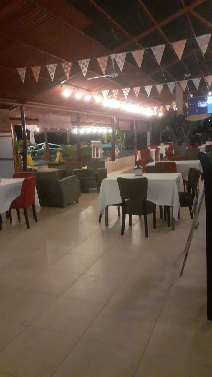 An outdoor dining area with tables and chairs, a covered section with a grill, and a view of the outside.