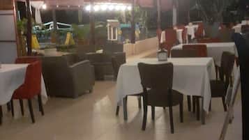 An outdoor dining area with tables and chairs, a covered section with a grill, and a view of the outside.