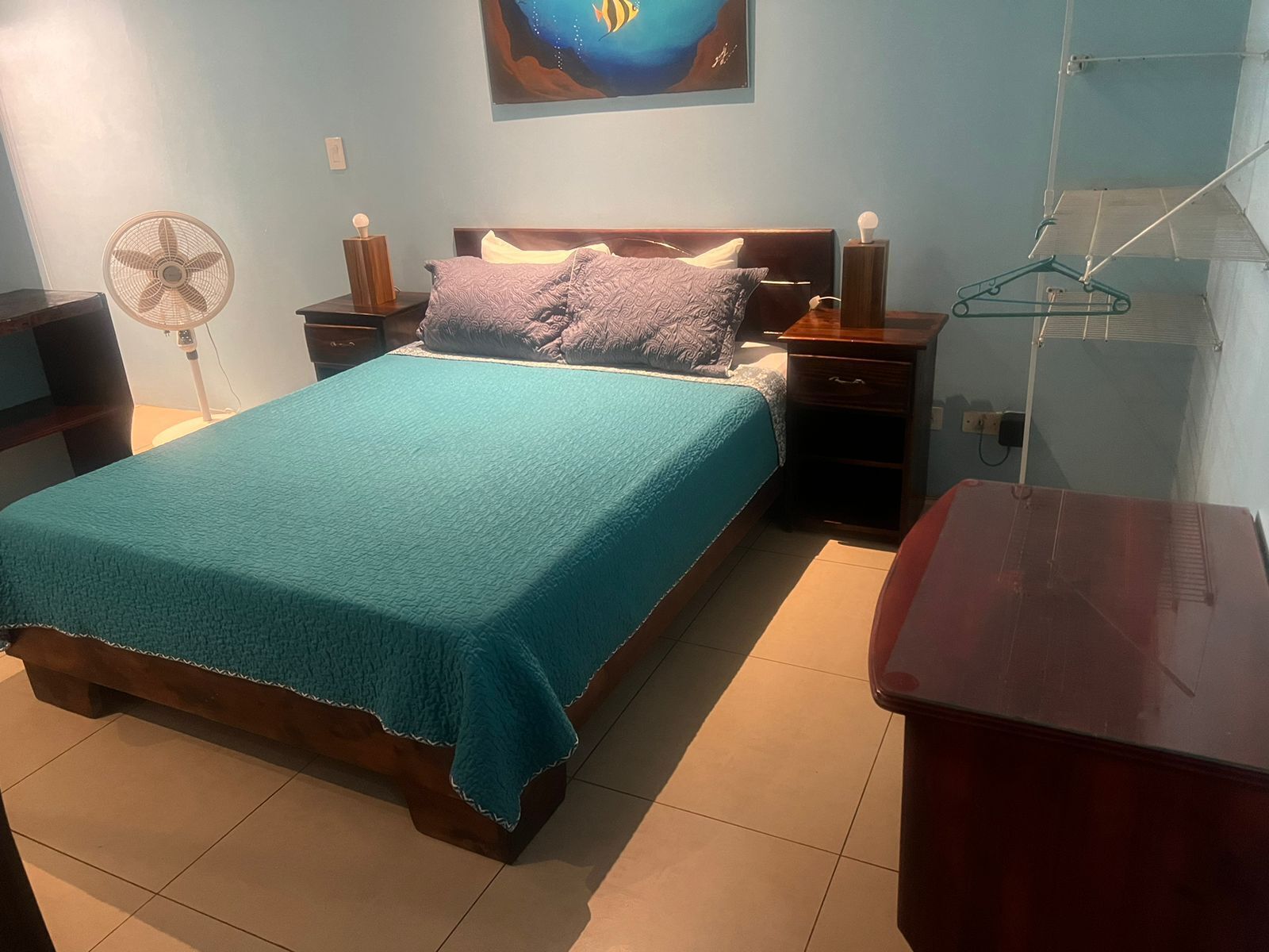 Un dormitorio con cama, mesitas de noche, ventilador, cómoda y estante en la pared.