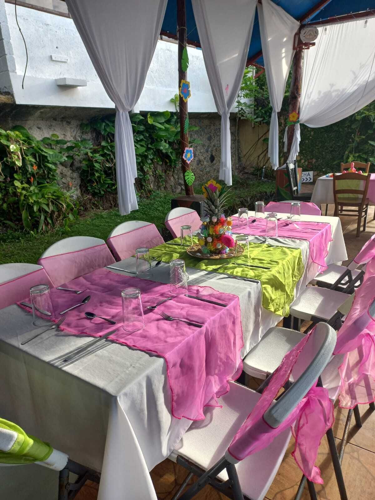 Een buitenterras met tafels voor vier personen, gedekt met witte en roze tafelkleden, omringd door stoelen.