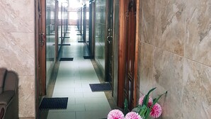 Corredor de hotel com paredes de mármore, portas de madeira e um tapete verde na entrada.