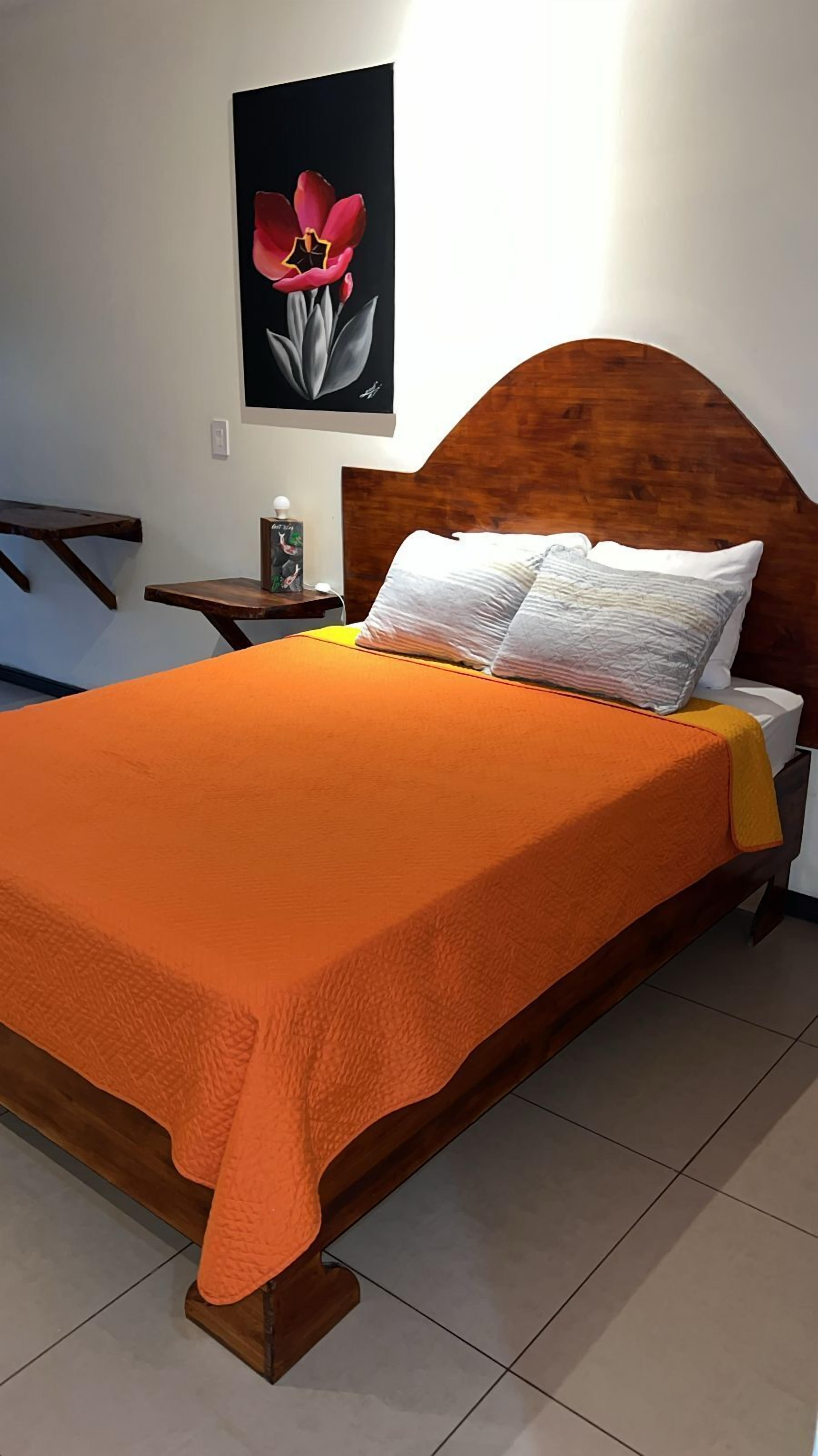 Une chambre à coucher avec une tête de lit en bois, une grande couvre-lit orange, des oreillers blancs et une table de chevet avec une lampe.